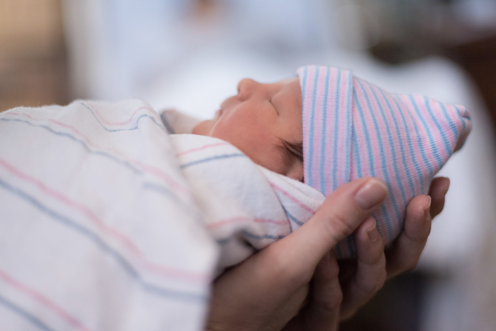 An adult holding a newborn in pijamas and a blanket