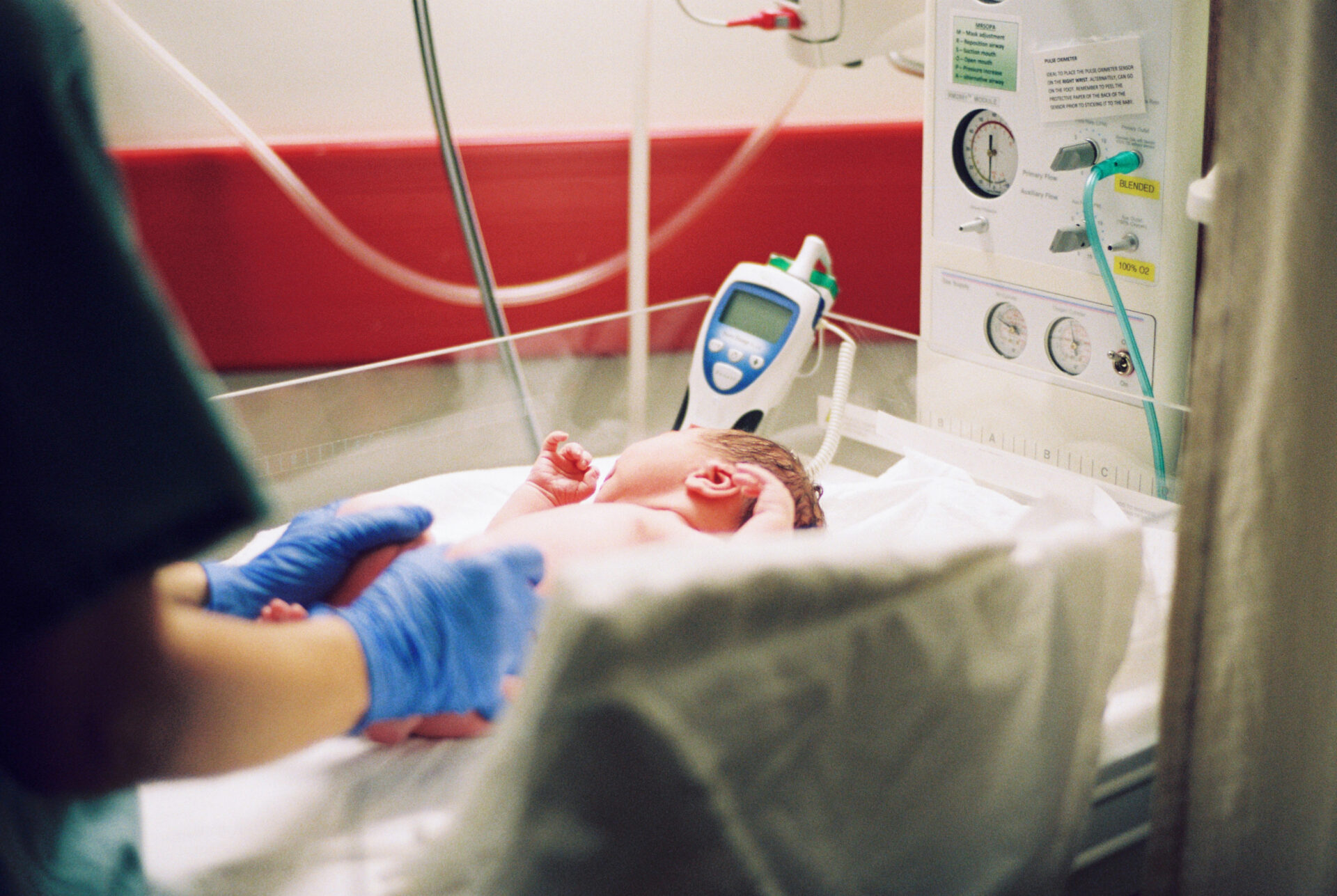 Nurse with blue gloves examining newborn baby in a newborn room