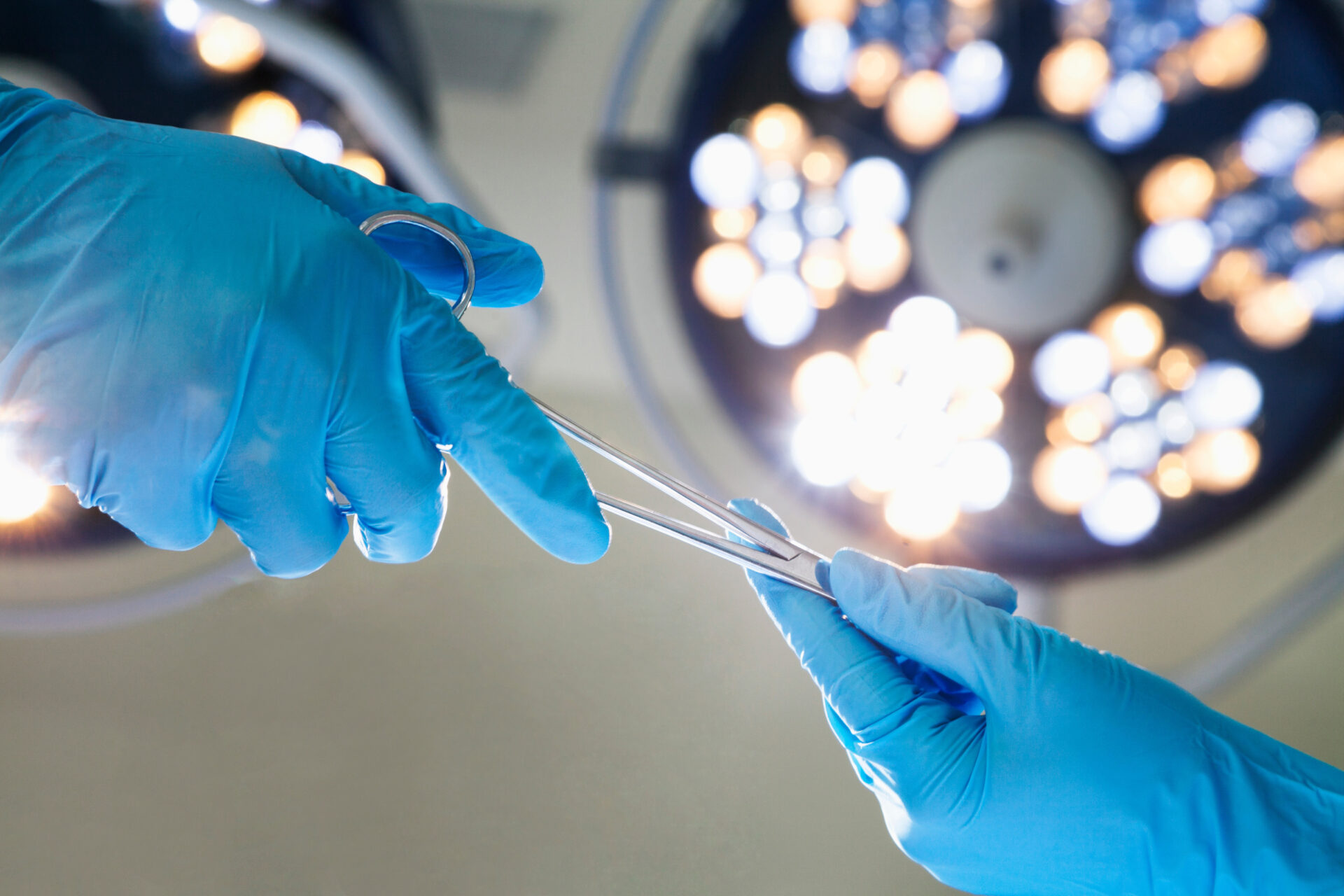 Two doctors in surgery wearing blue gloves, holding medical tweezers