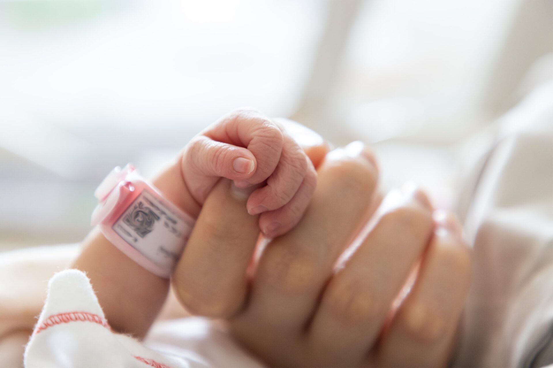 Newborn baby holding an adult's hand with a hospital bracelet visible | Recognizing symptoms of hypoxic ischemic encephalopathy in newborns, medical malpractice law, medical procedure - The Pagan Law Firm