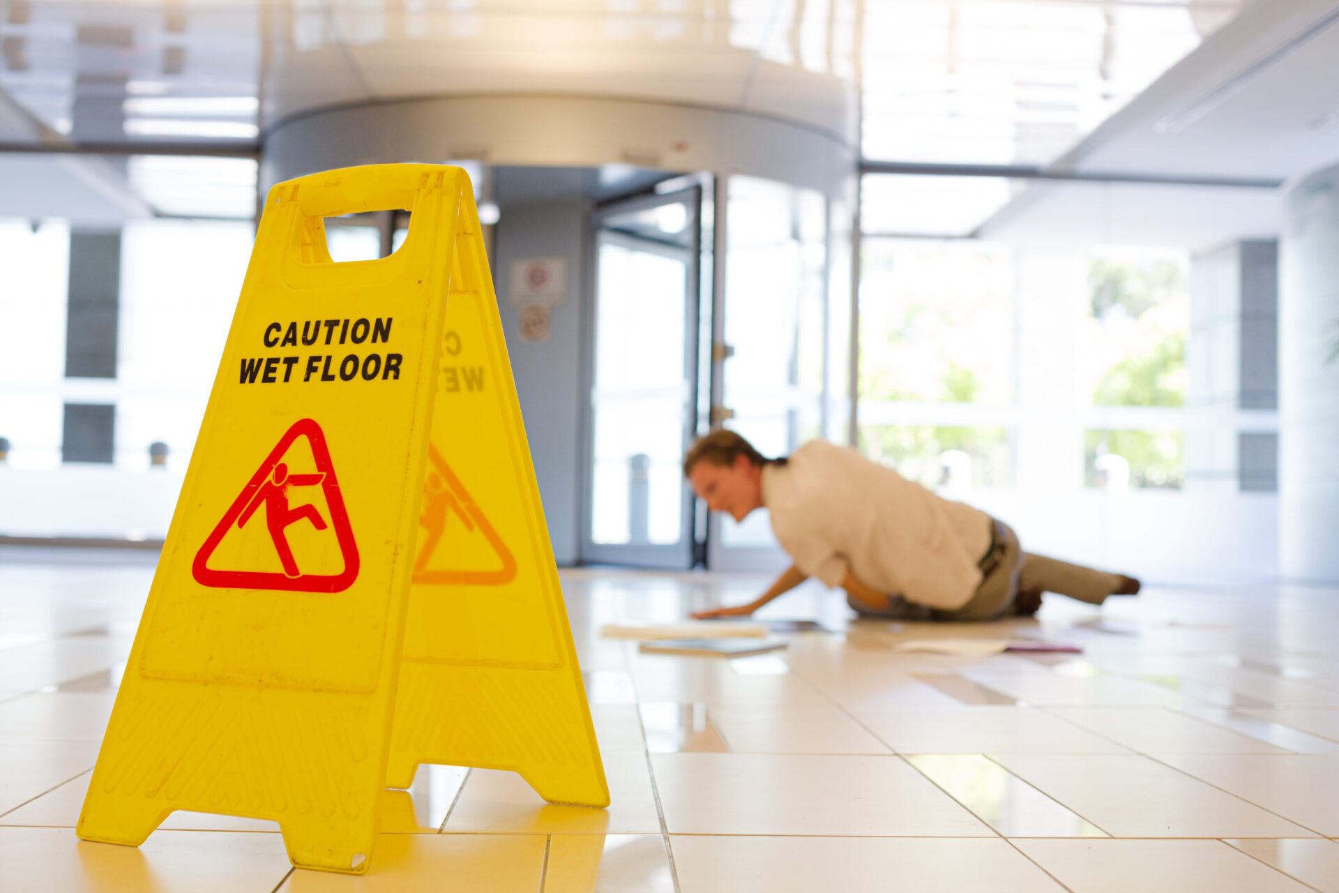 Yellow caution wet floor sign with a person slipping in the background | Slip and fall lawyer - The Pagan Law Firm