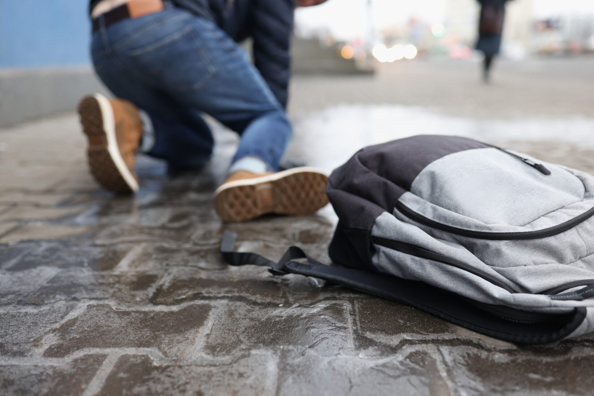 Injured person on wet pavement after a slip and fall accident, with a backpack in the foreground. The Pagan Law Firm can help victims seek compensation.