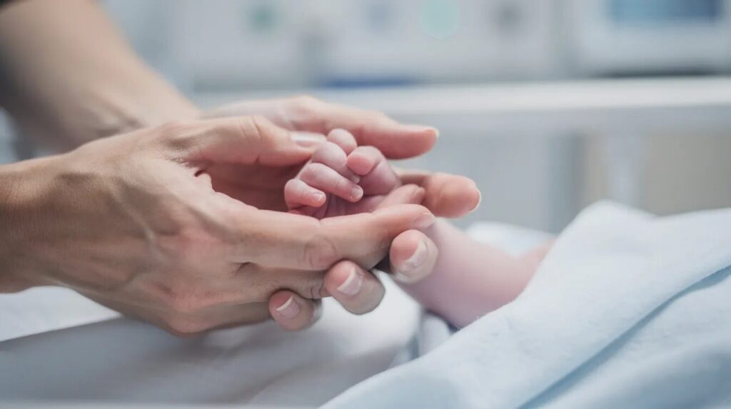 In a hospital setting, a parent gently holds their newborn baby's tiny hand, symbolizing the bond of care and protection. The image evokes the importance of monitoring bilirubin levels to prevent complications like severe jaundice, which can lead to serious medical conditions if untreated.